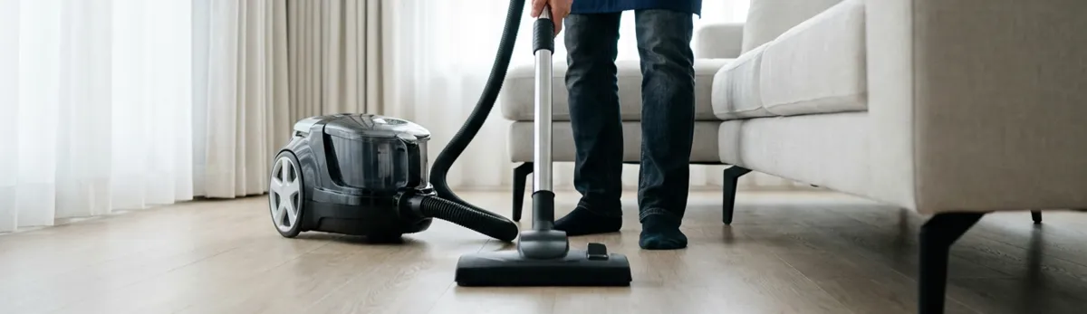 Professional house cleaner vacuuming a living room floor with a canister vacuum cleaner, Springfield, MO.